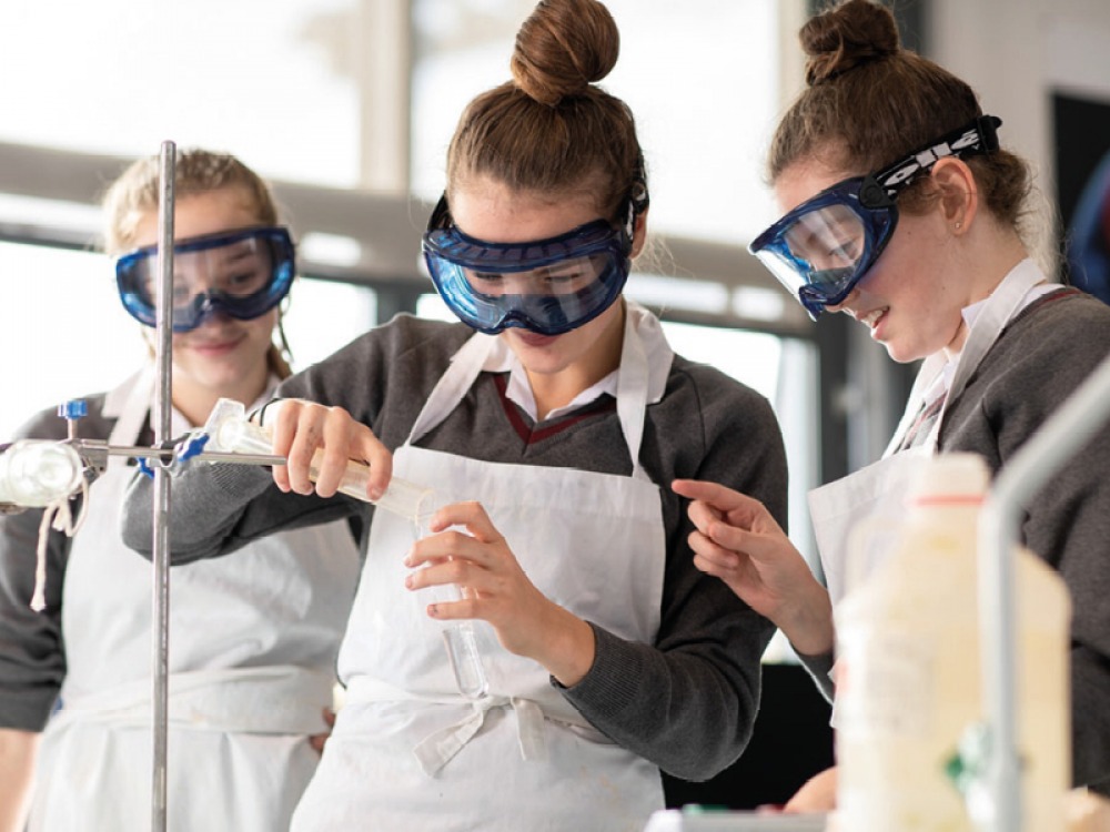 female students wearing aprons and safety googles carrying out an experiment