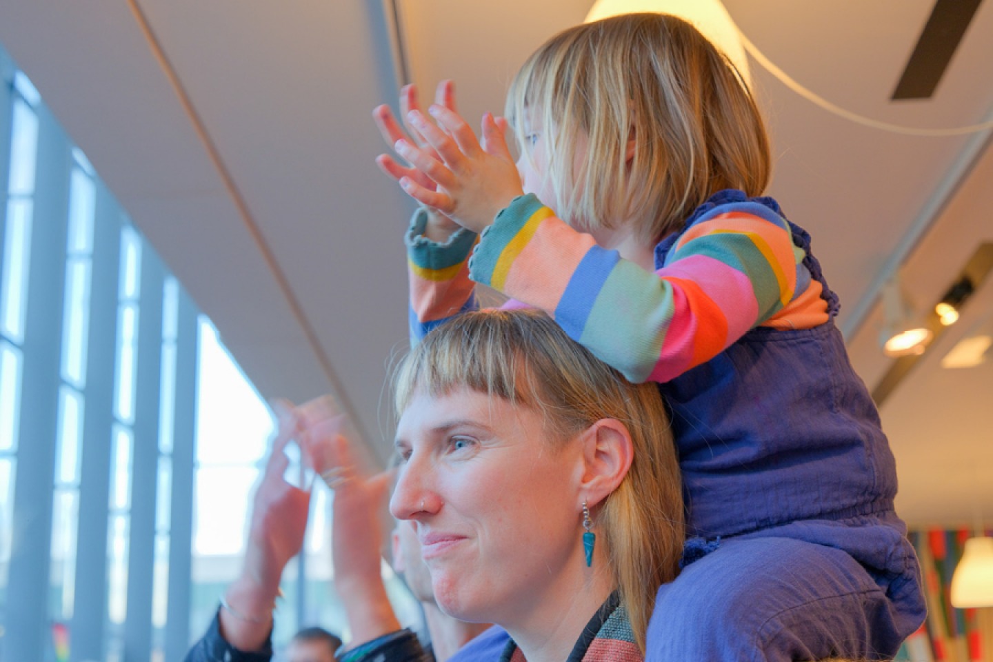 young girl on mothers shoulders clapping hands
