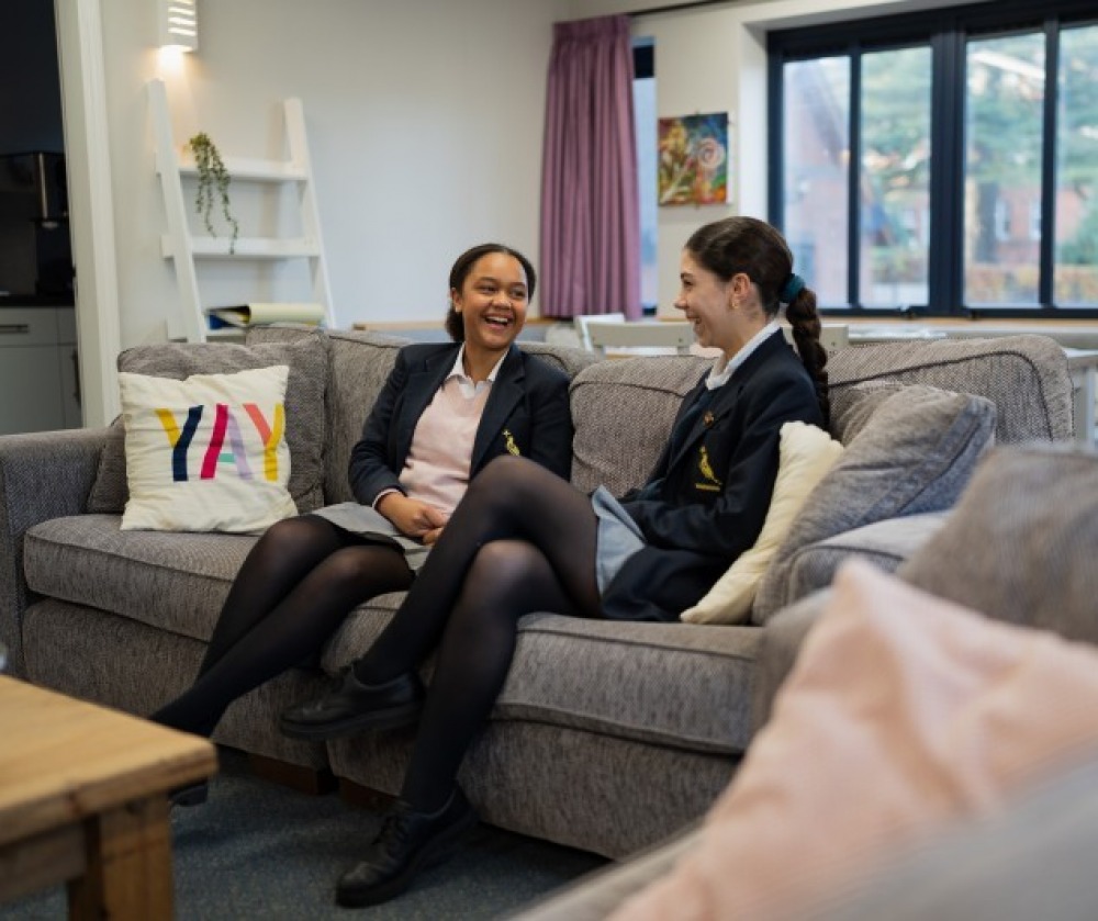 Two female pupils sitting on a couch conversing