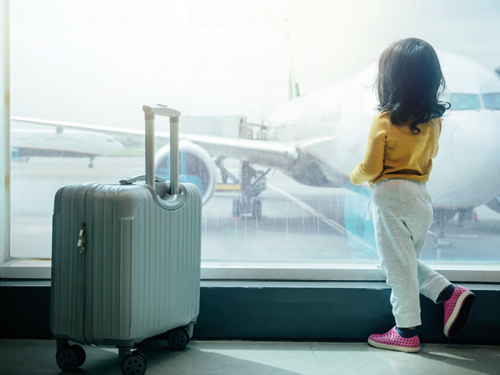 Child at airport standing with case looking out at the aeroplanes