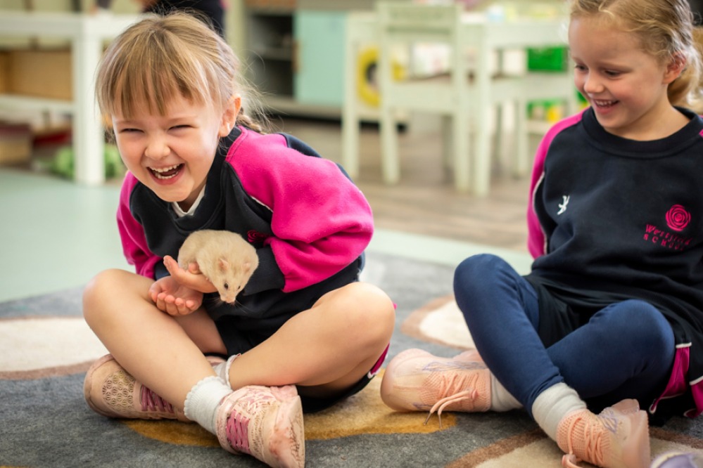 2 young girls giggling one handling a hamster