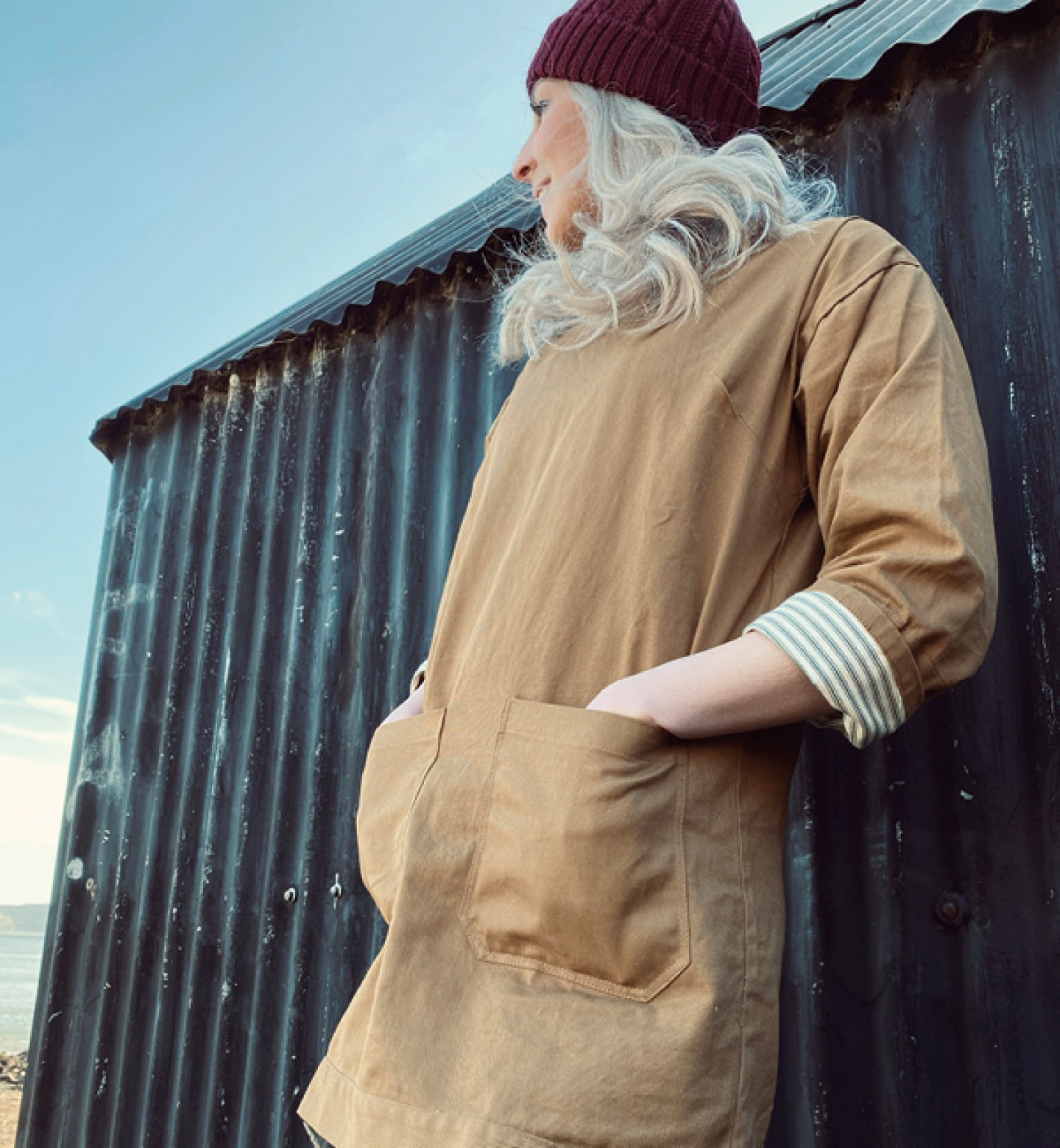 woman wearing beanie hat and beige coat leading against corrugated shed