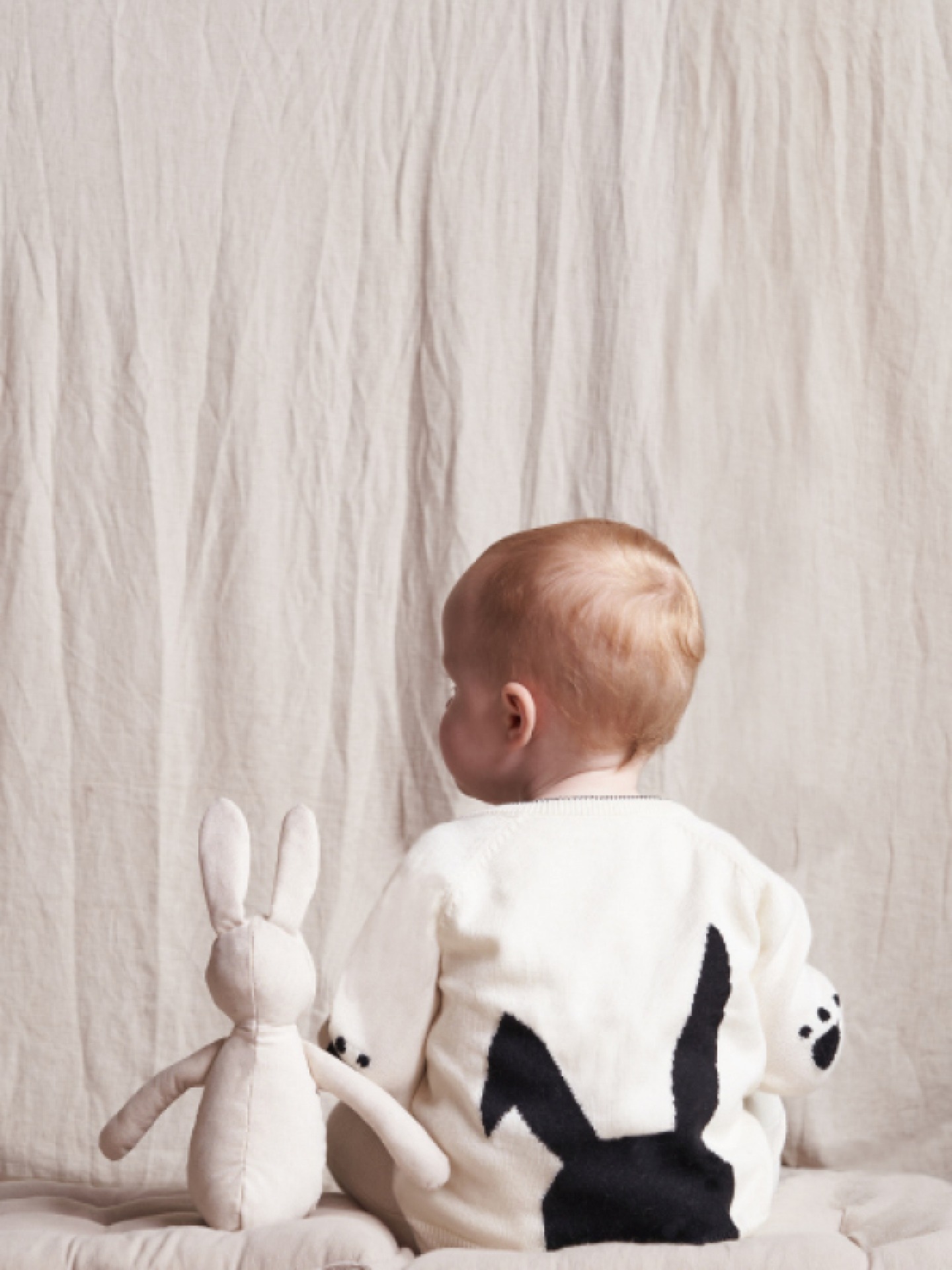 Photo of a toddler from behind sitting next to a plush bunny