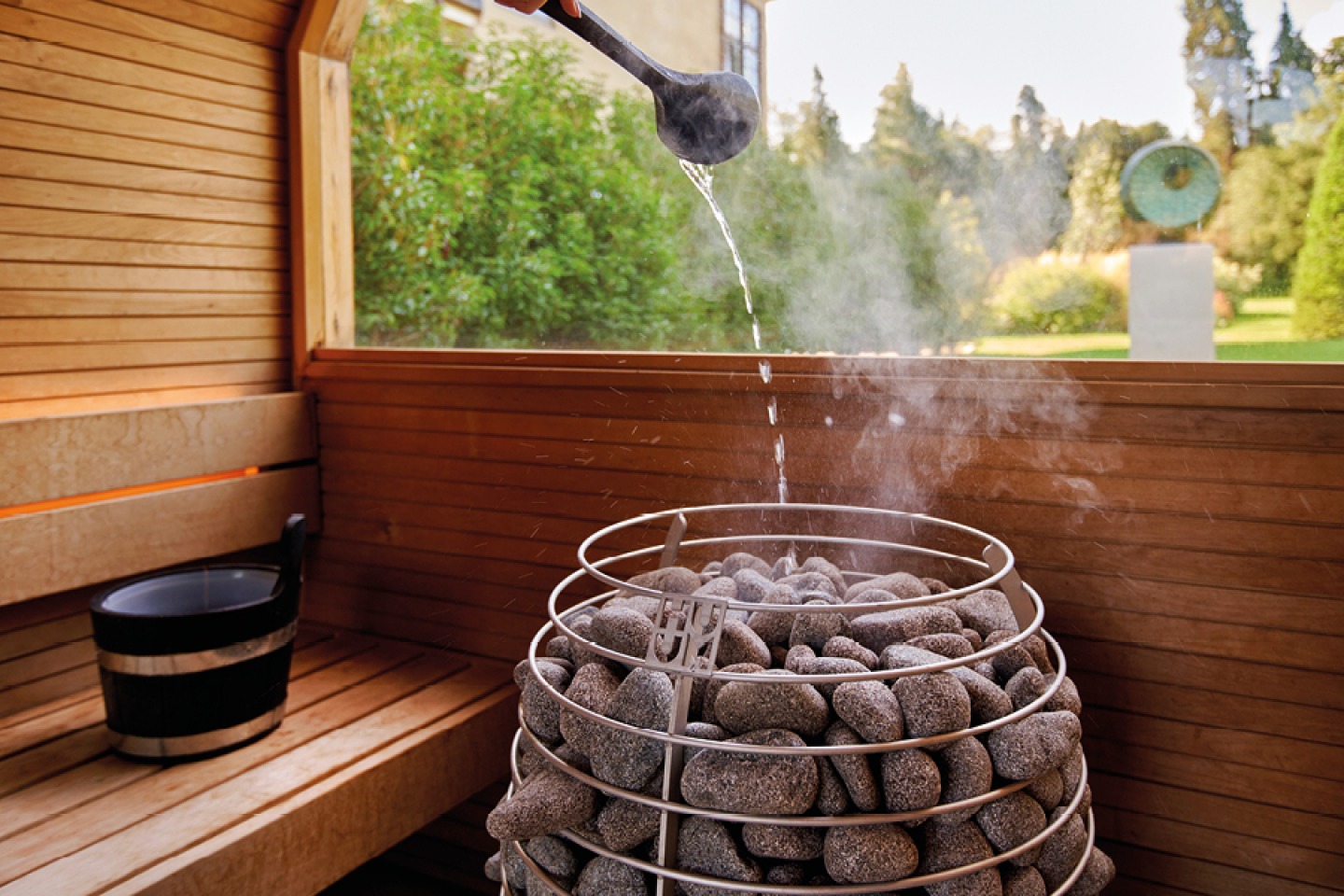 water being poured from a spoon into hot stones in a sauna