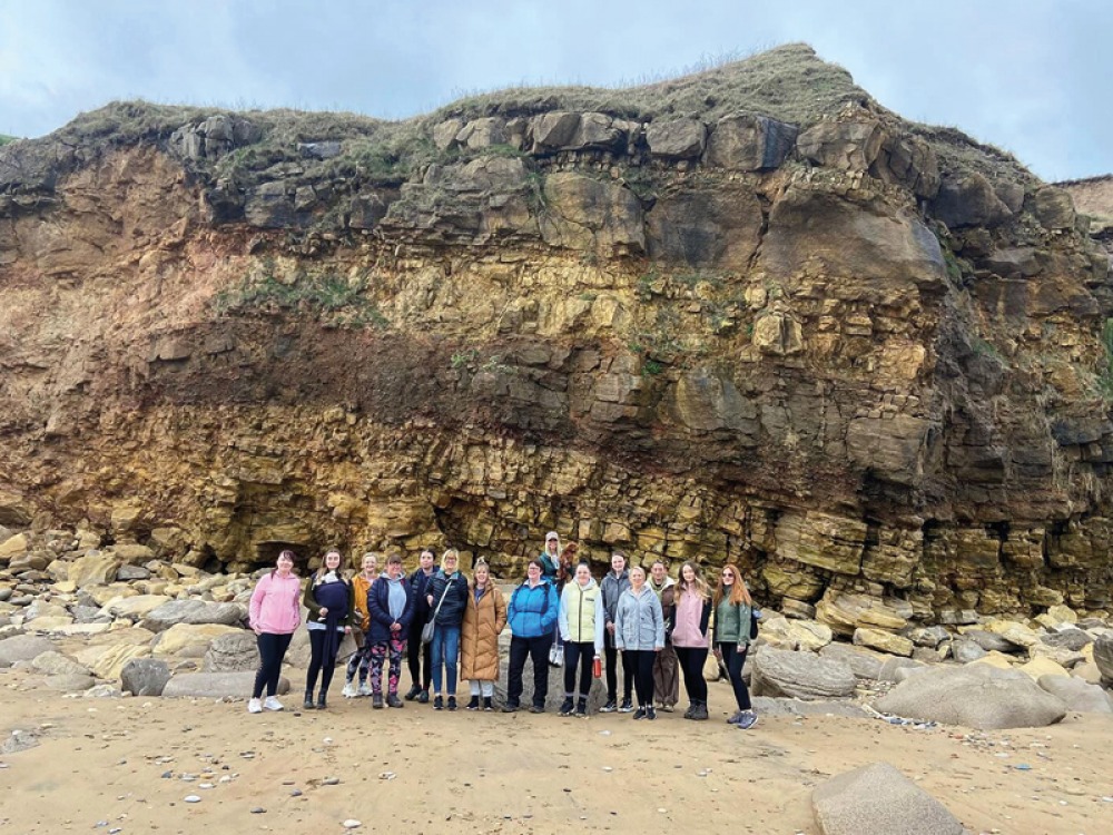 group of women lined up for a photo on the beach in front of a rocky cliff edge