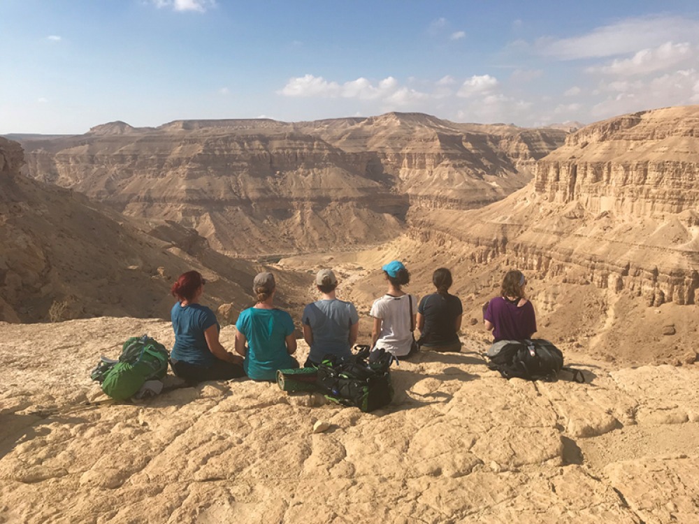 group of women sitting on a cliff edge looking over mountains
