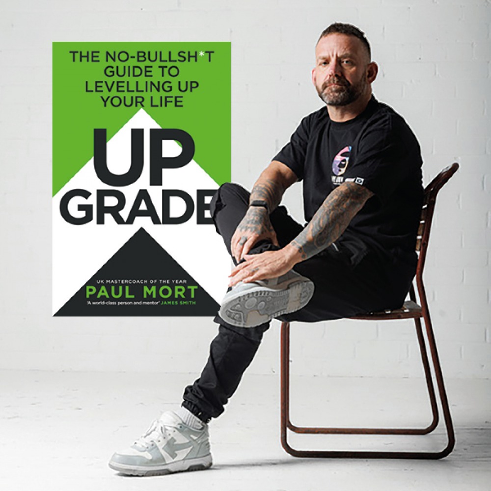 Paul sitting on a chair with a large cover of his book behind him