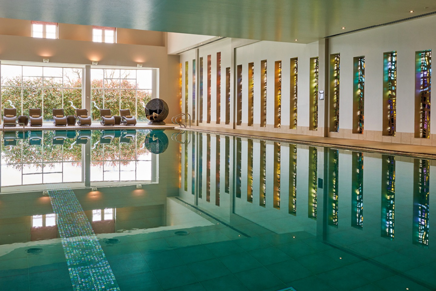 Swimming pool with large glass windows and lounger seating