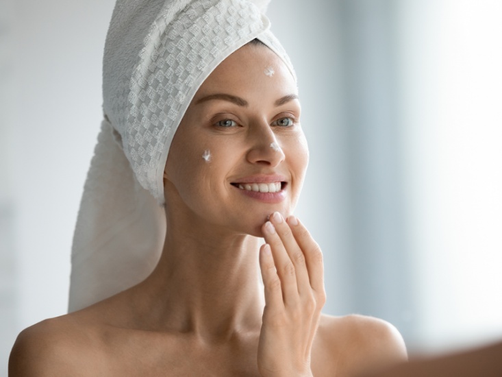 woman applying moisturiser on her face in front of a mirror
