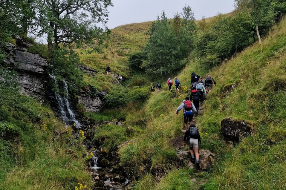 people scrambling up grassland near a waterfall