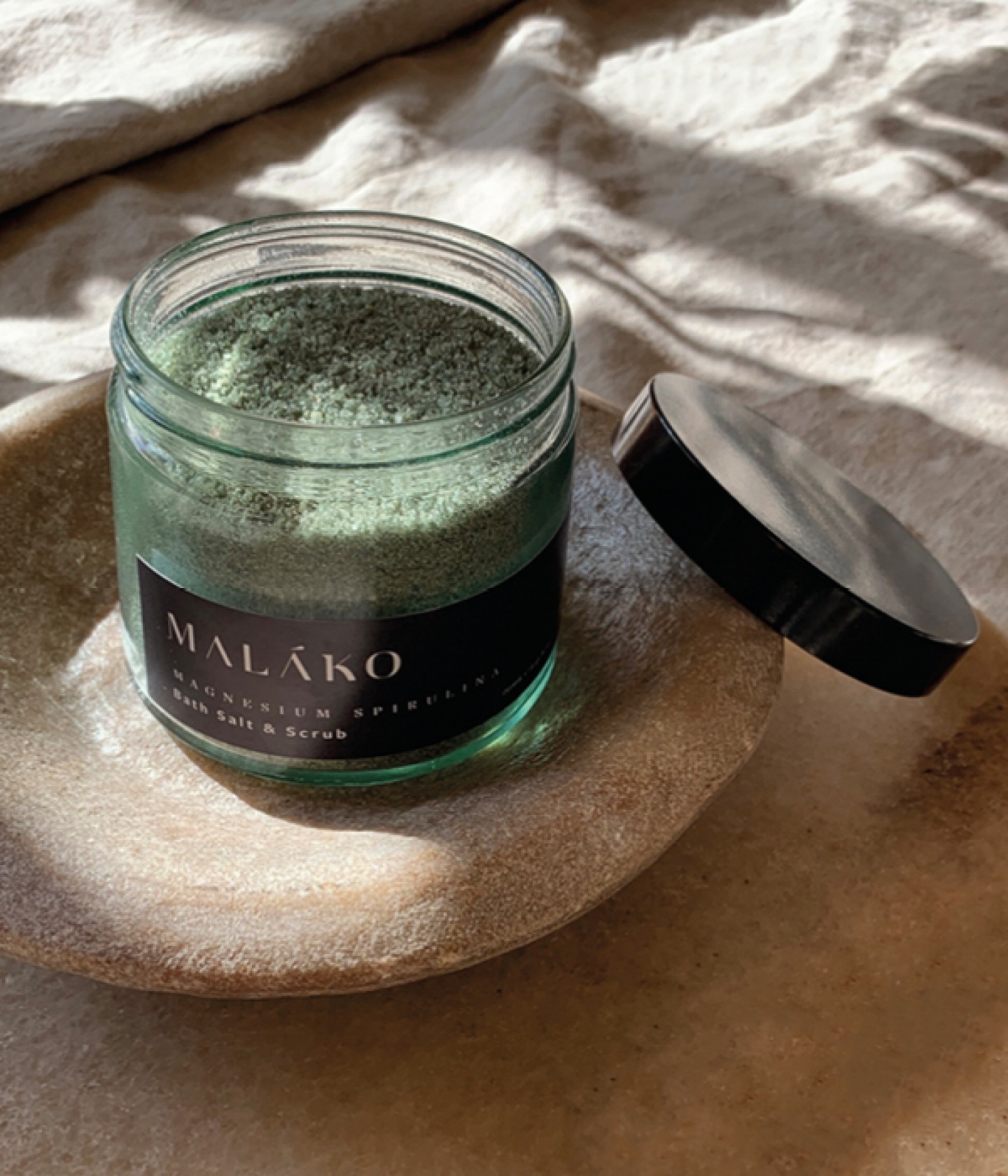 jar of open body scrub sitting on a stone dish