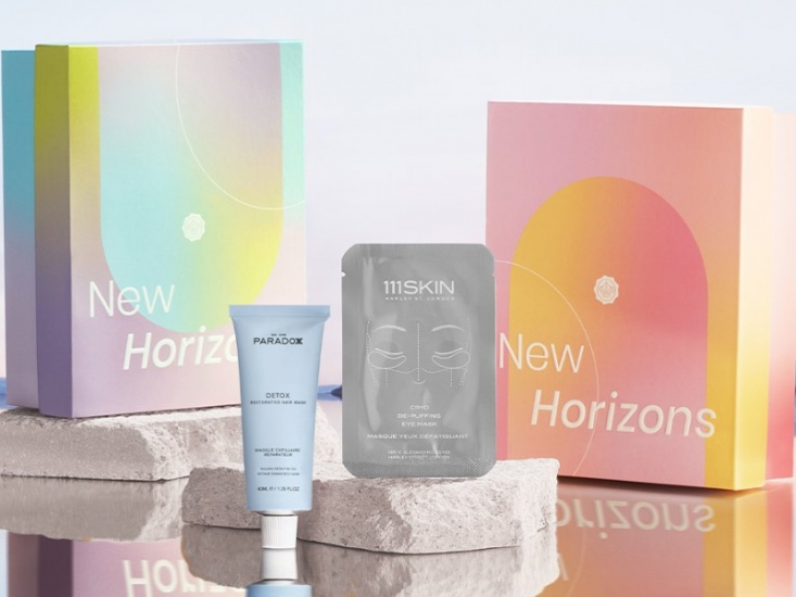 Two multicoloured Glossyboxes side by side with a blue tube in the foreground and a grey under eye mask