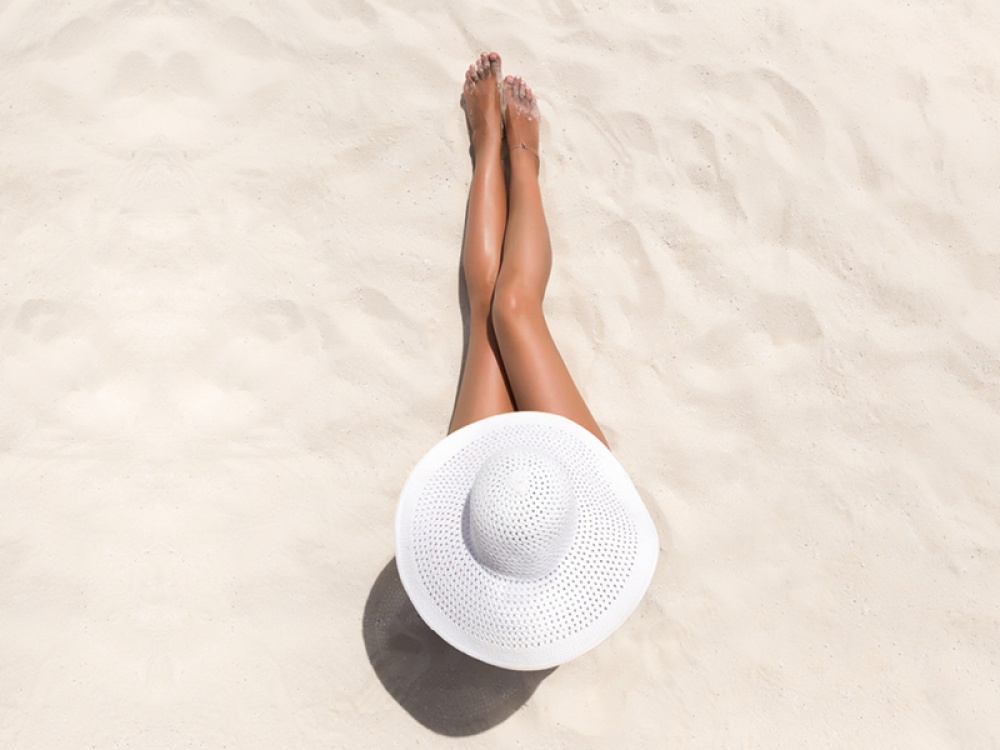 Ariel view of a woman lying on a beach wearing a sun hat with her legs stretched