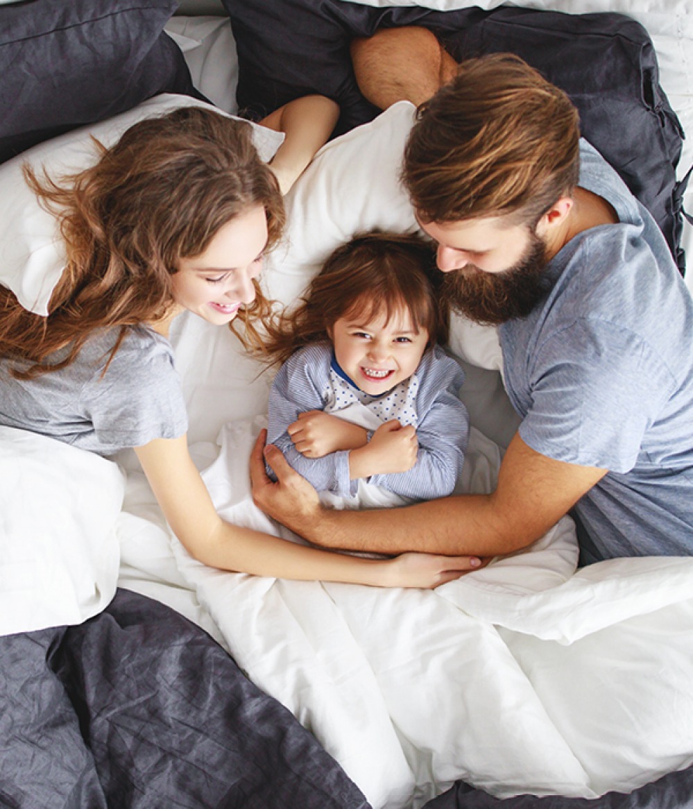 mother, father and daughter snuggling in bed