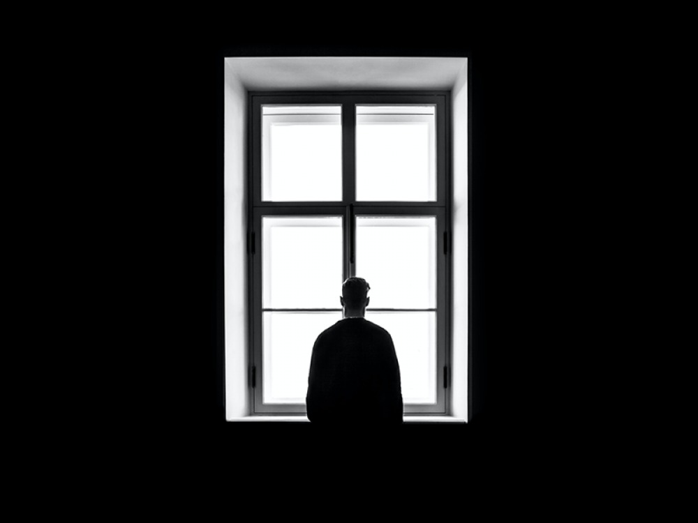 Black and white image of a man looking out a window at nothing