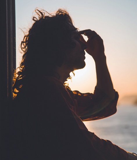 Man sitting at an open Window at sunset with his hand on his face