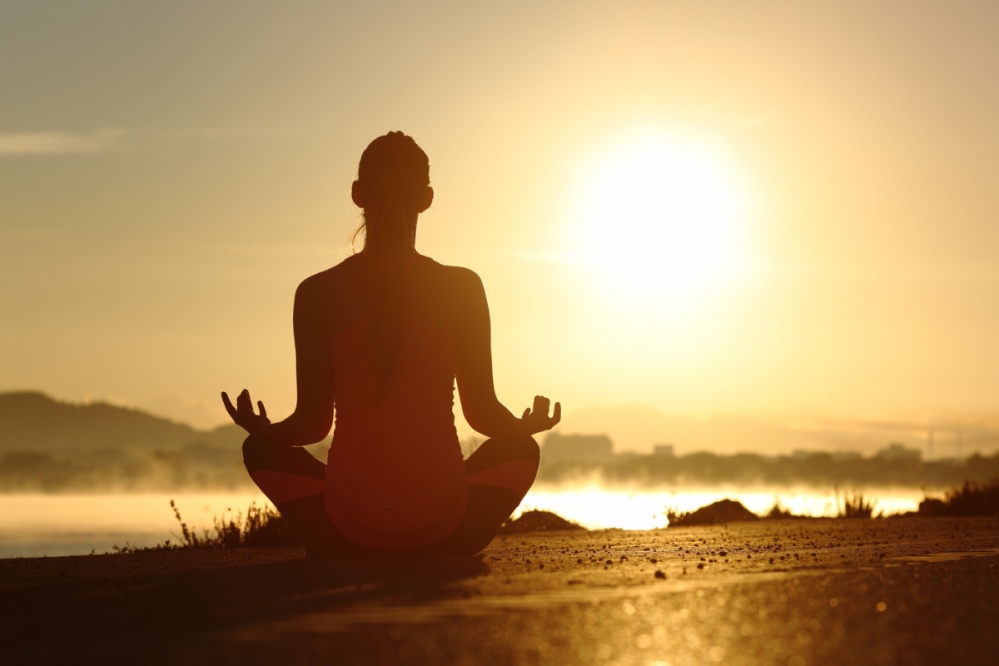 Silhouette of a woman meditating with the sun in the background