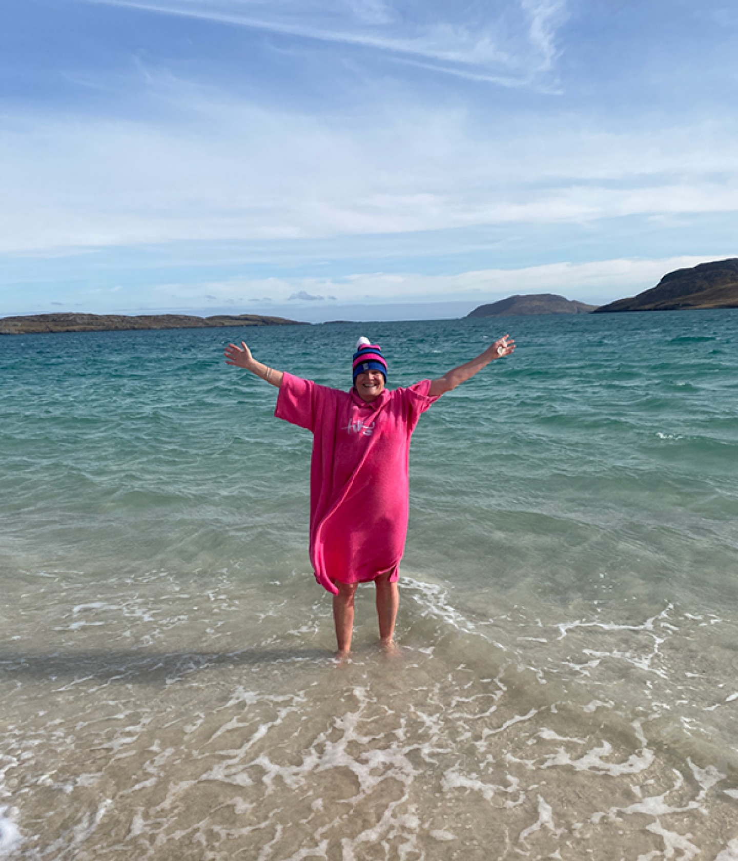 Siobhan standing in the sea with a poncho towel and a woolly hat