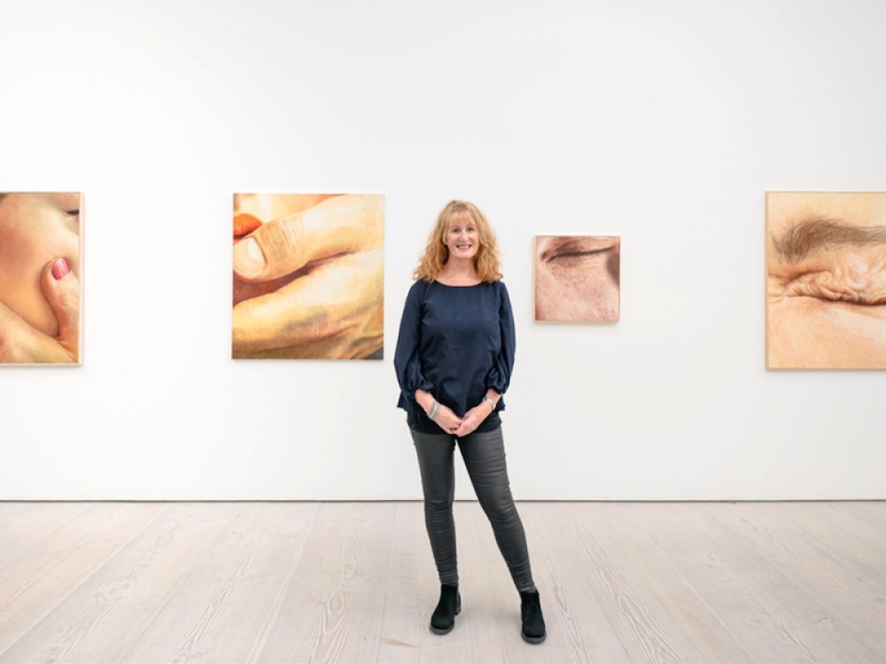 woman wearing a blue top in front of her paintings