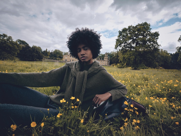 woman wearing a dark green cashmere jumper in a field of yellow flowers