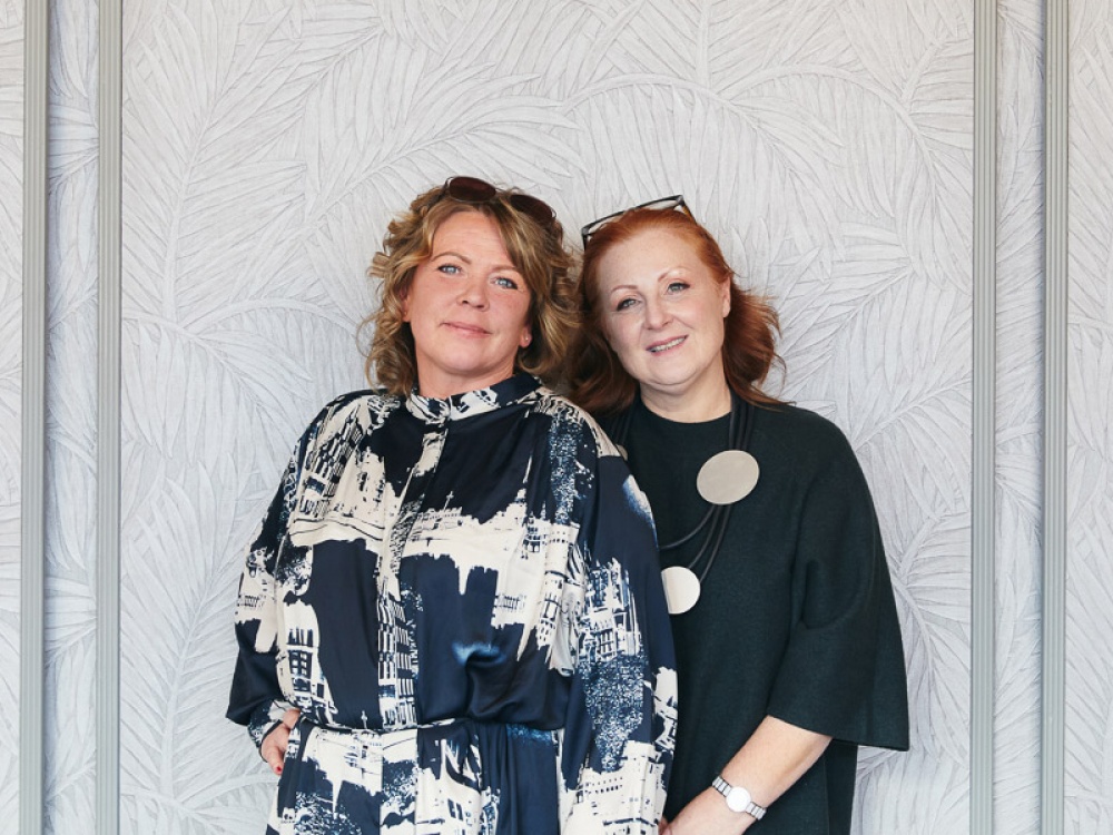 two women smiling for a photo in front of a wall