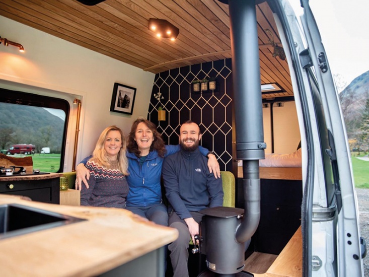 3 people smiling sat in a camper van