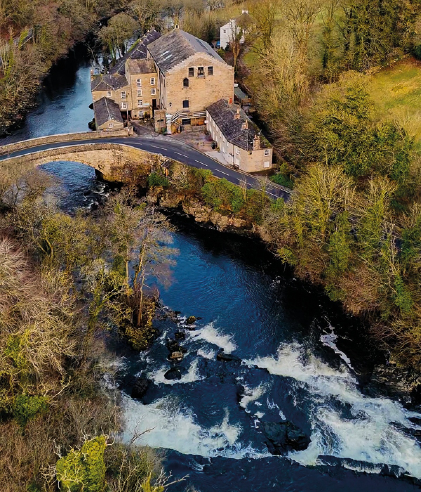Ariel view of a large stone building at the river edge with a large stone bridge