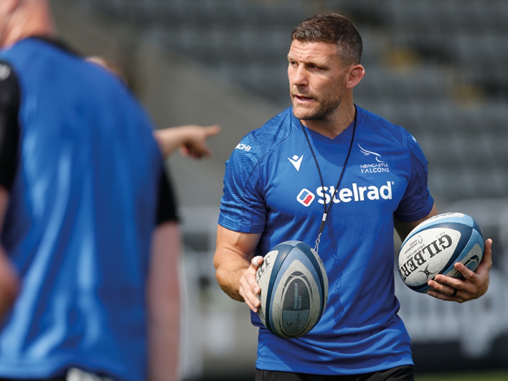 man wearing a blue top holding a rugby ball