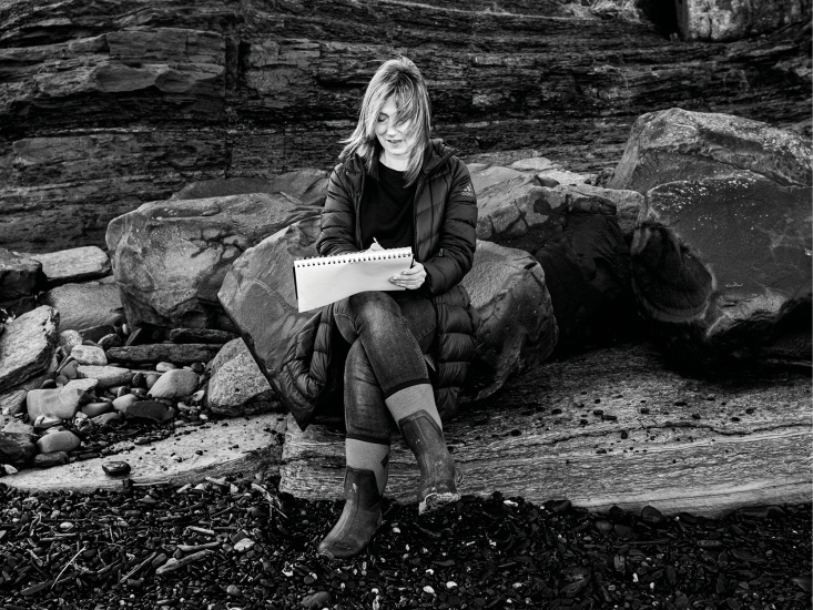 Katherine Renton sitting on rocks drawing