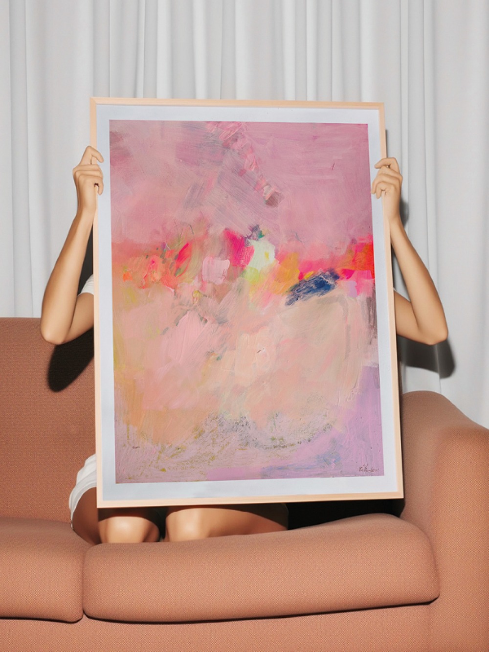 Kirath sitting on a couch holding a framed painting in front of her