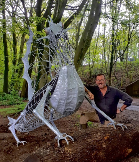 Graeme Hopper kneeling next to his sculpture of a dragon