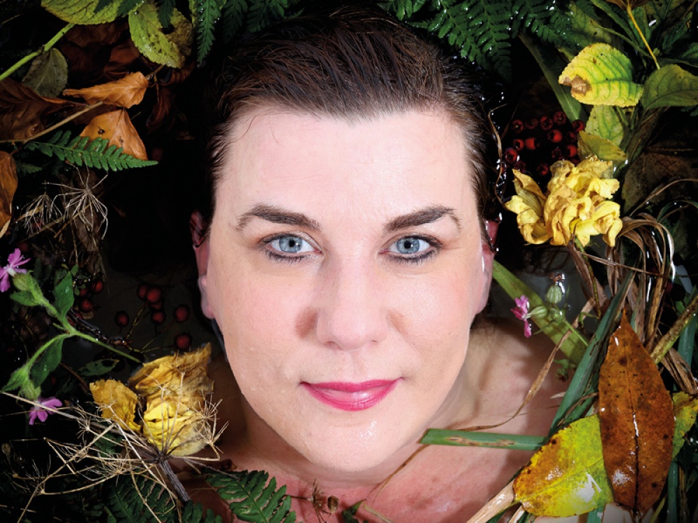Kate Fox Face poking through water surrounded by flowers, leaves and greenery
