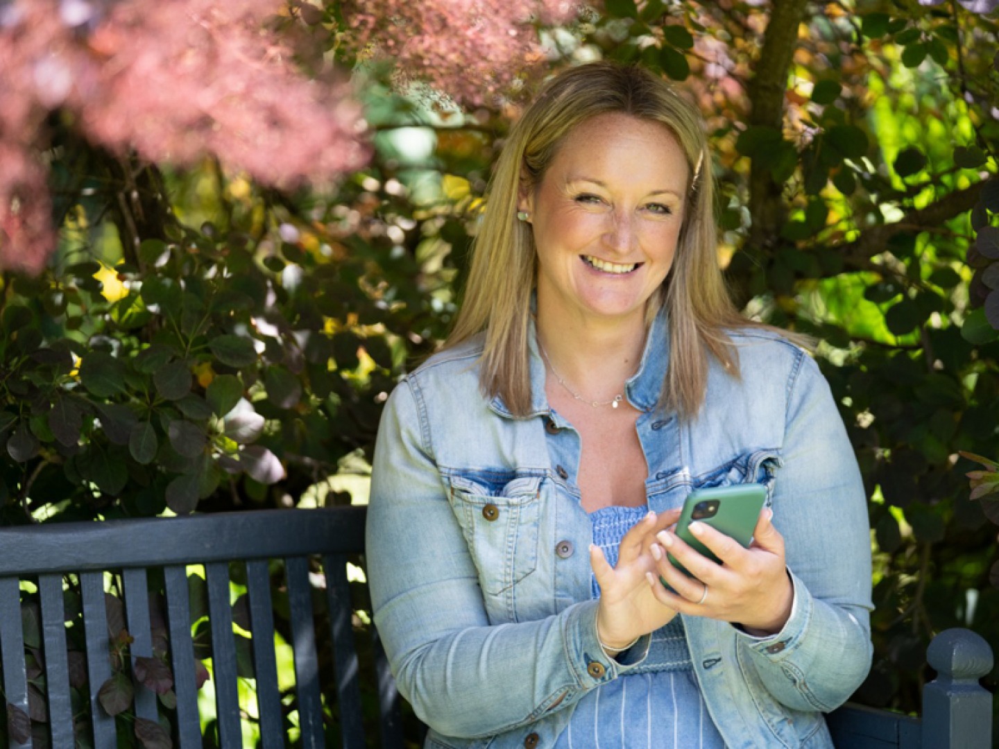 portrait of a women sitting on a bench under tree blossom using a mobile phone