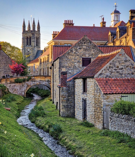 stone buildings near a stream, stone bridge and a church in the background