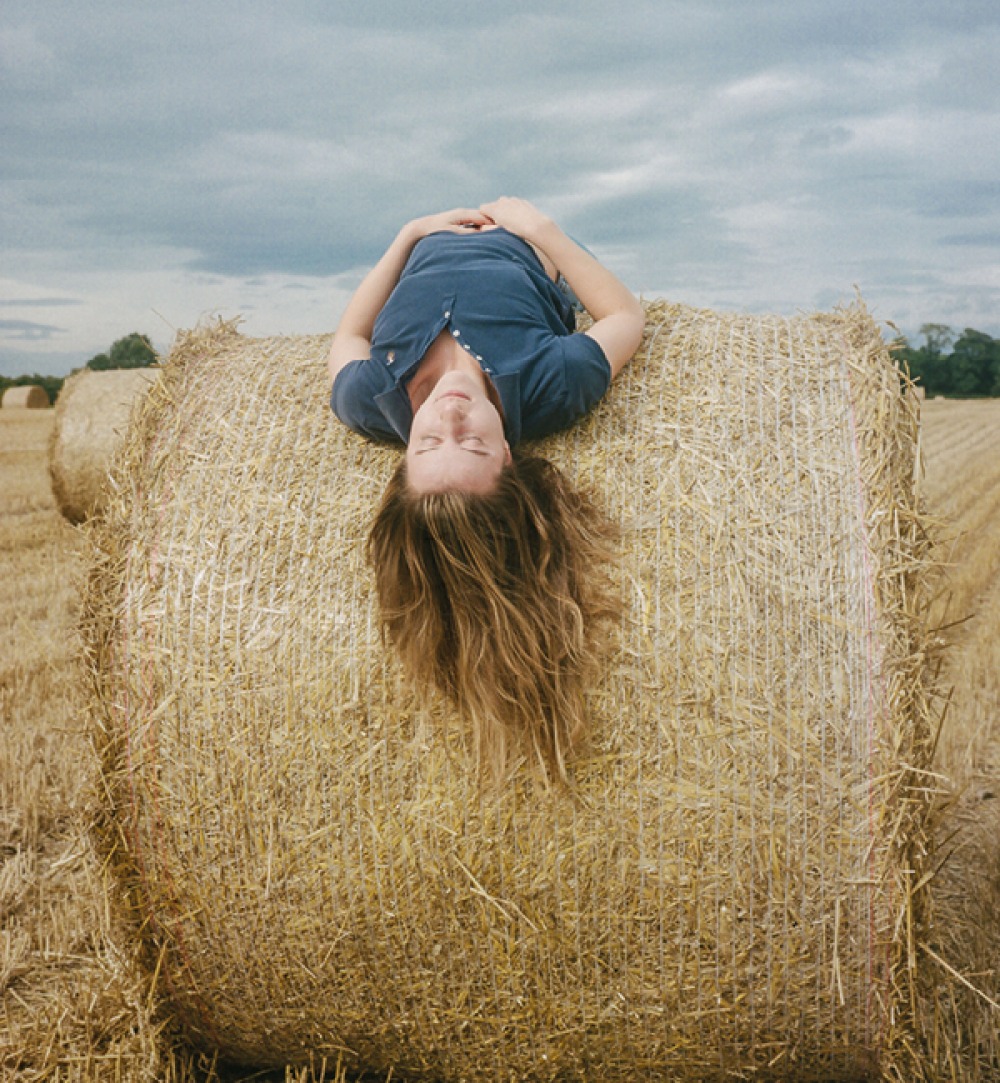 woman lying over bale of hay