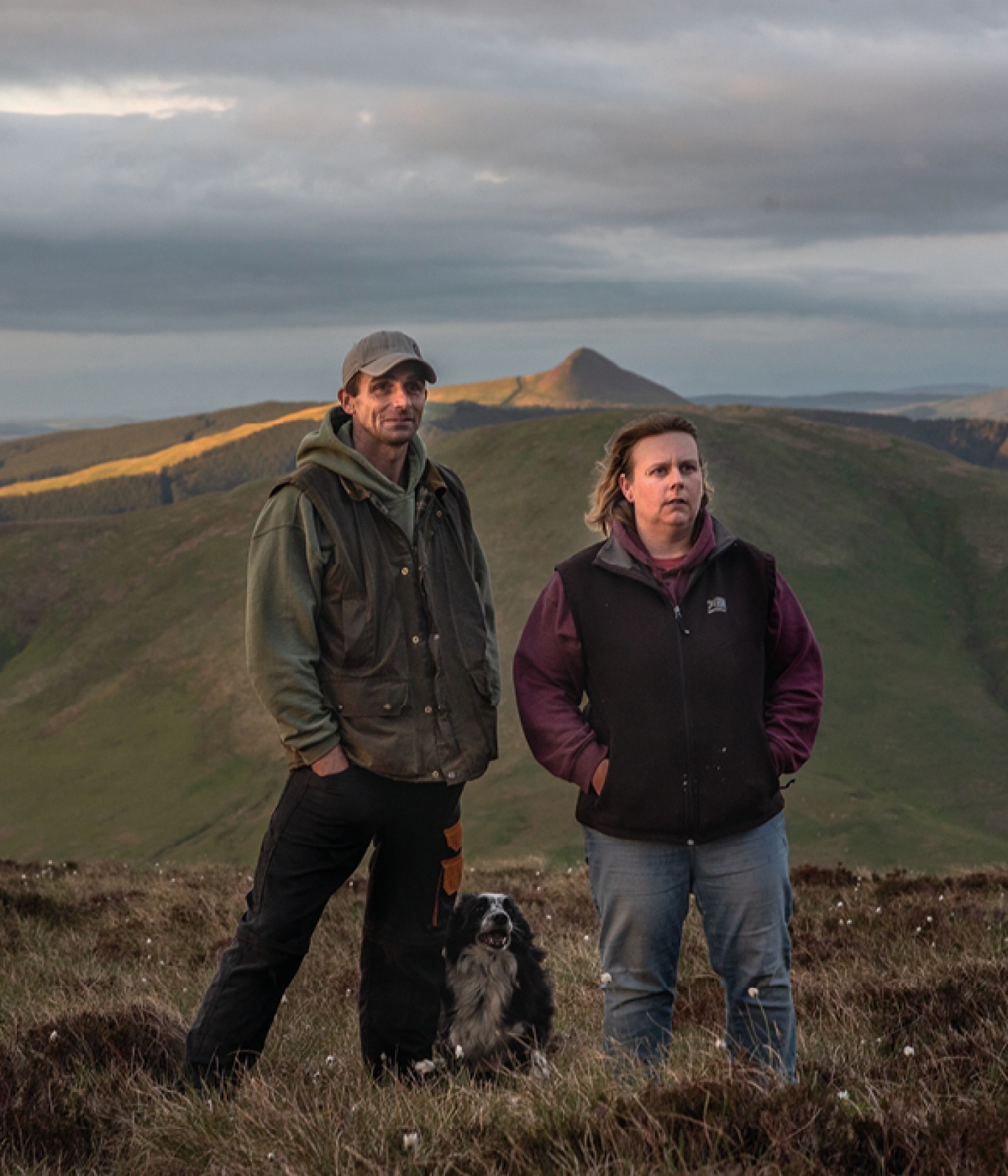 man and woman standing with their dog in hills