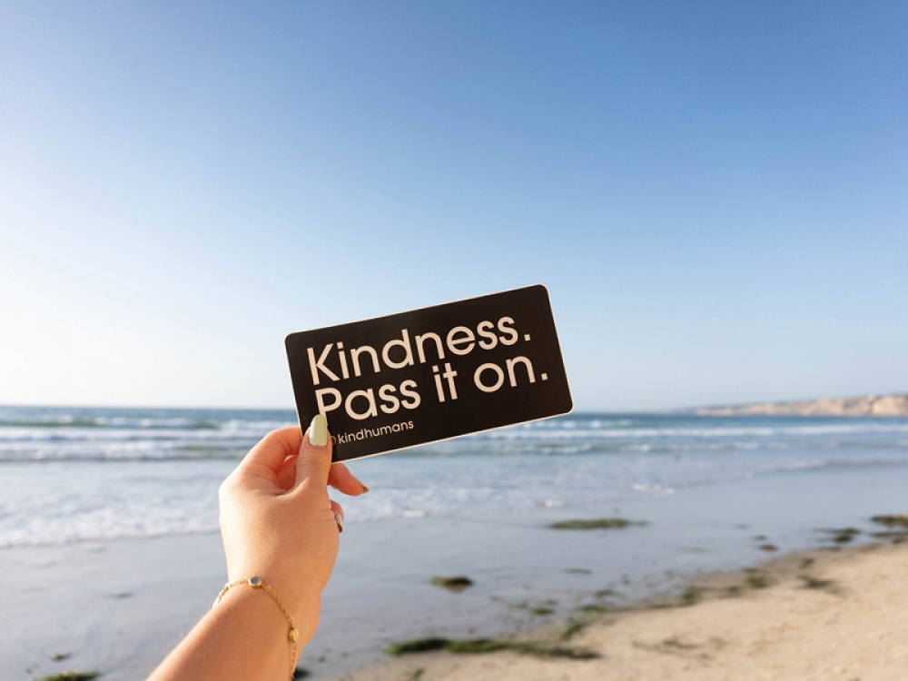 hand holding a note that says KINDNESS.Pass it on.