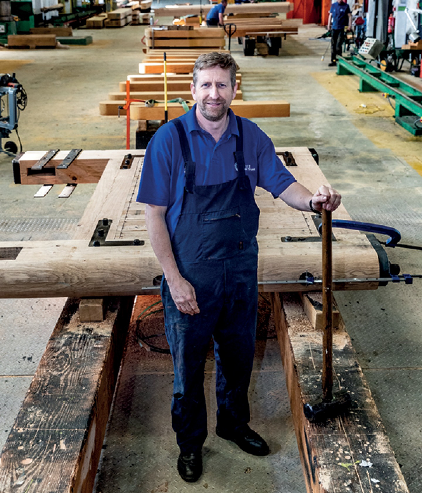 Man standing in a factory posing infant of gates with a hammer