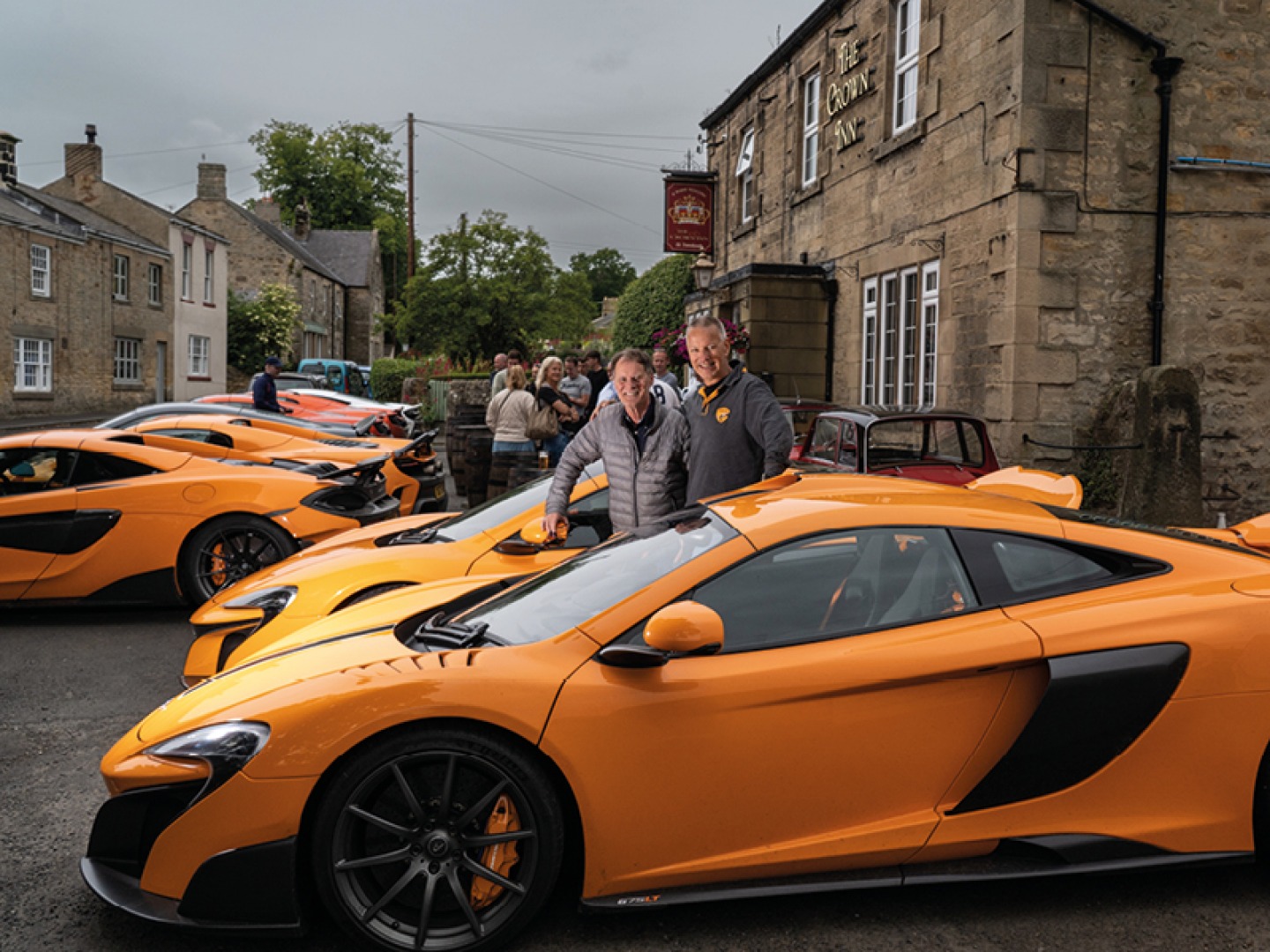 2 men standing in behind an orange Mclaren outside the Crown Inn