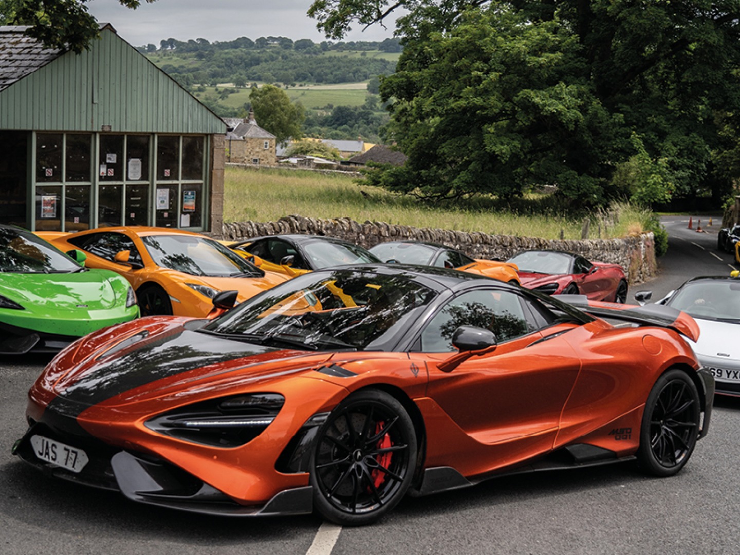 Mclarens parked up with a burnt orange one driving past