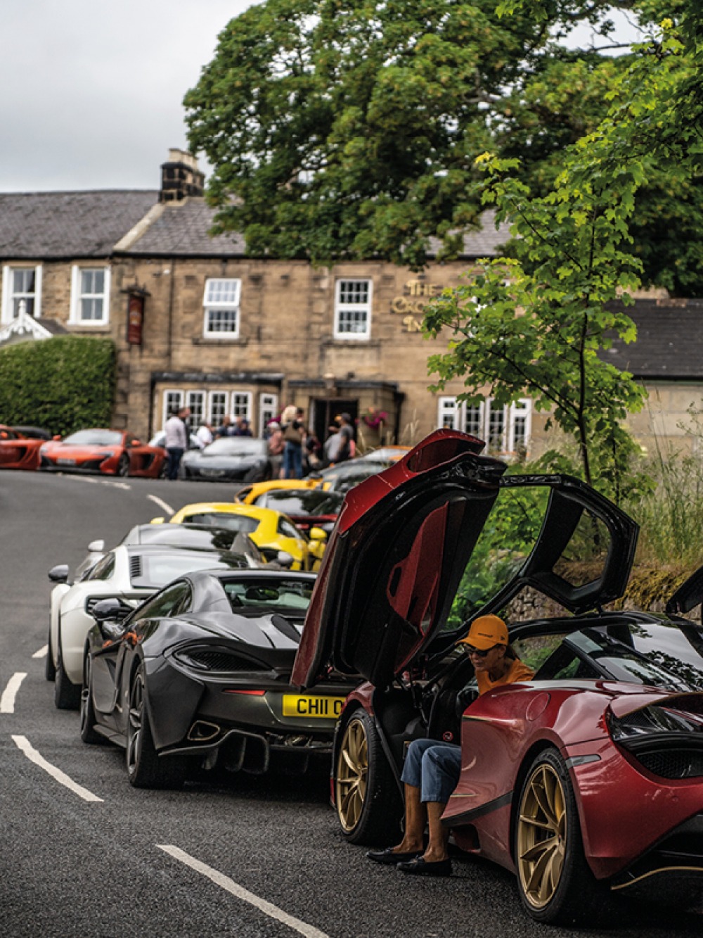 woman climbing out of a Mclaren with others parked up