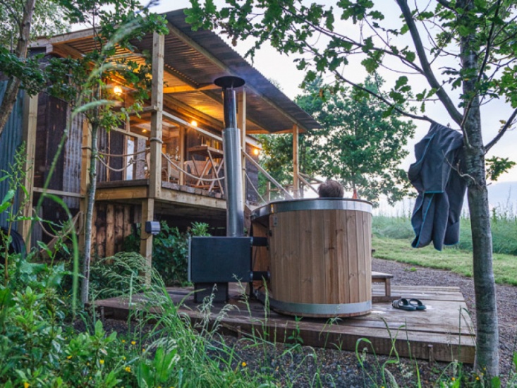 Man in an outdoor hot tub looking a wooden cabin