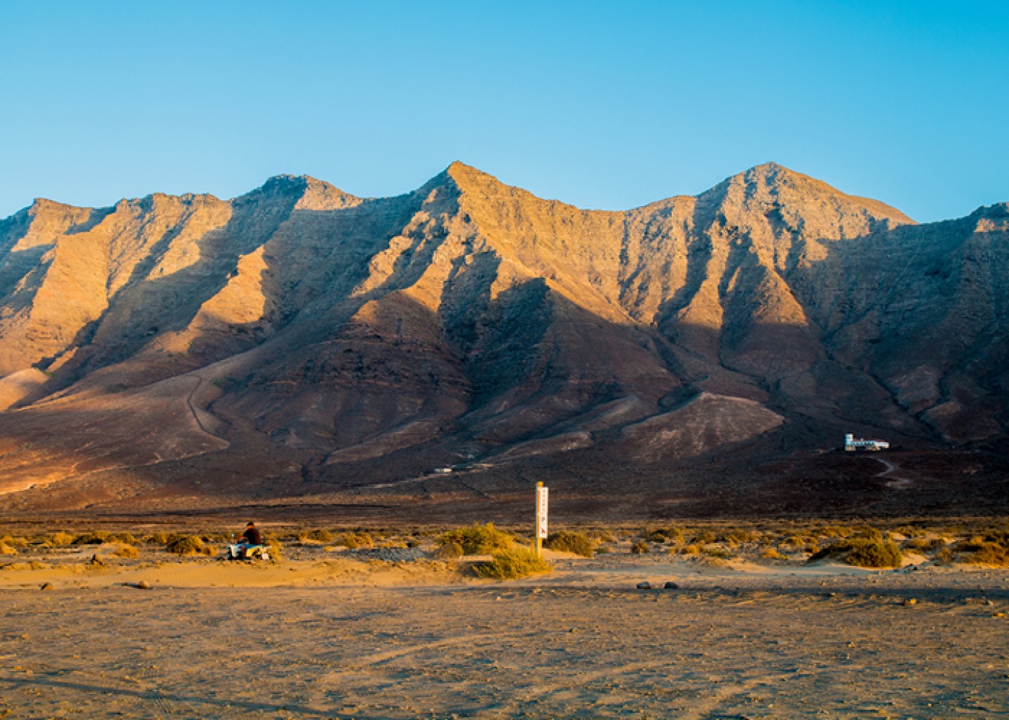 quad bike driving through open dessert land with Mountains with blue sky