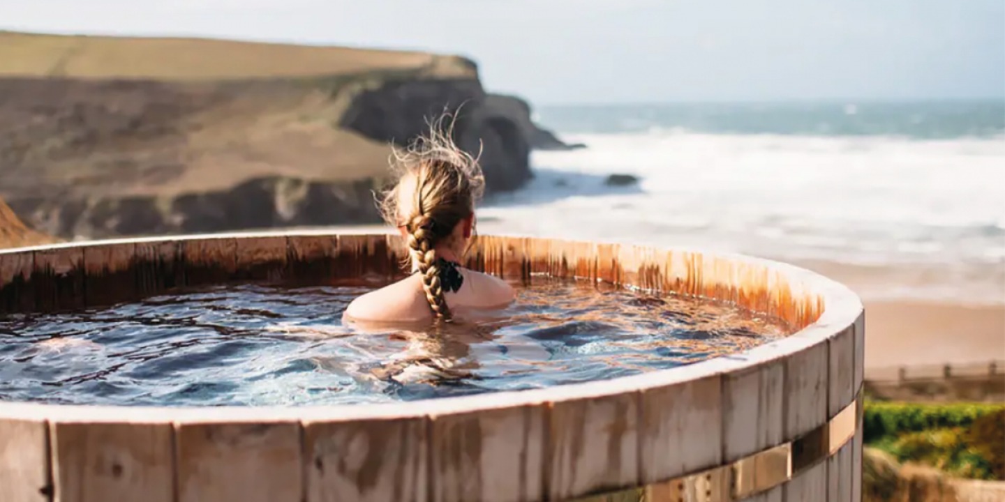 Girl in a wooden hot tub looking over the cliffs and sea