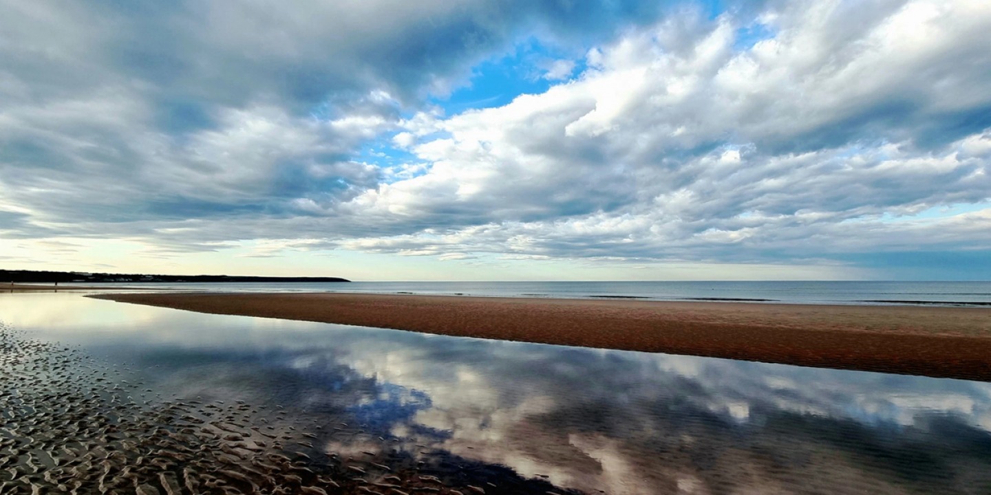 Shallow waters at the beach reflecting the blue sky and clouds