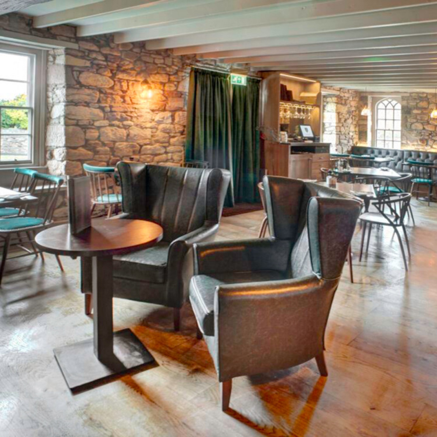 2 large leather arm chairs around a small round table in a pub with exposed stone walls and low beamed ceiling
