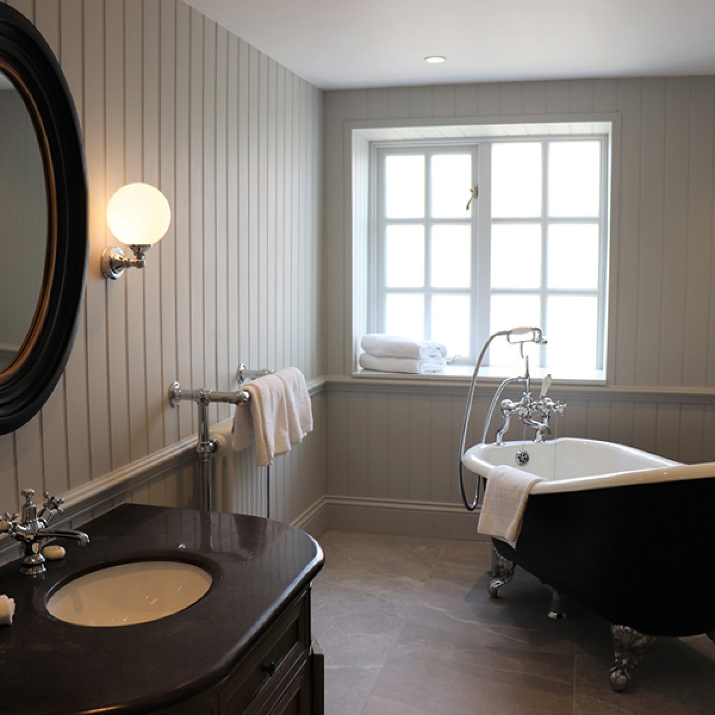 Bathroom with free standing roll top bath with wall paneling and traditional radiator and sink