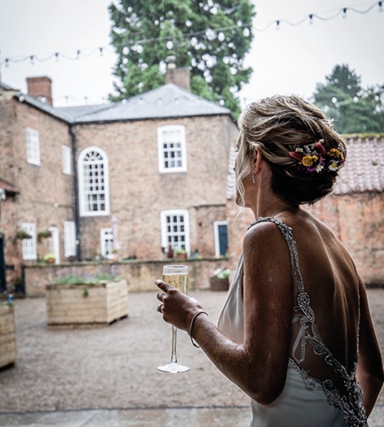 back of the bride looking out over courtyard holding a glass of fizz