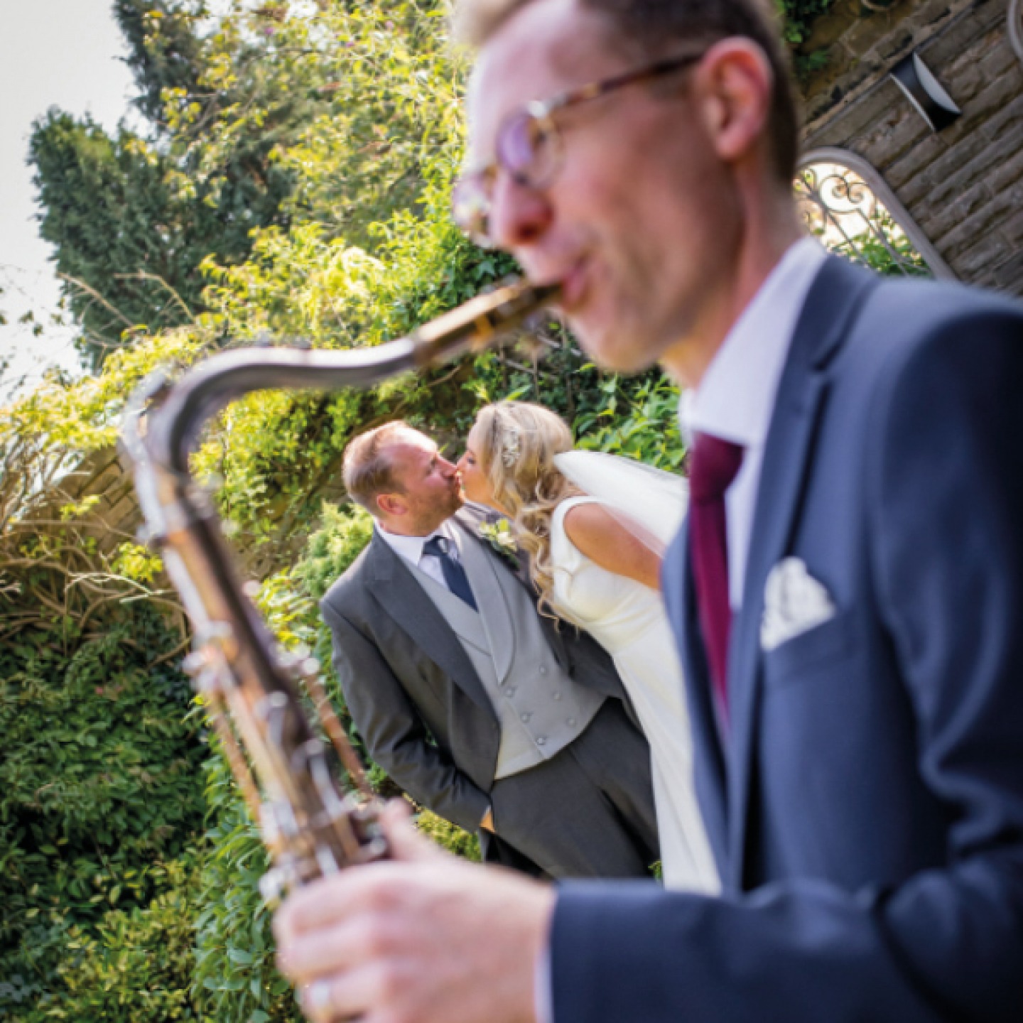 bride and groom kissing with saxophonist in foreground
