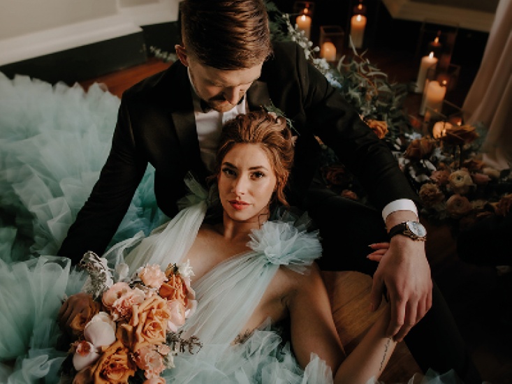 Bride and groom posing together on the floor surrounded by flowers and candles